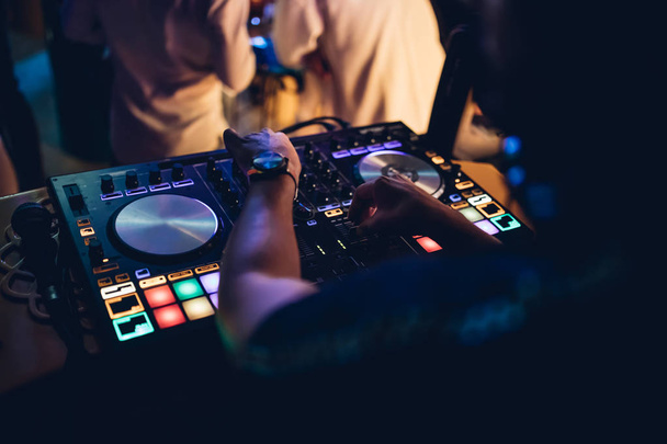 Ο DJ παίζει live set και αναμιγνύει μουσική σε πικάπ στη σκηνή του night club. Disc Jokey χέρια σε ένα σταθμό μίξερ ήχου στο κόμμα club. DJ πίνακα ελέγχου μίξερ για αναπαραγωγή μουσικής και πάρτι. - Φωτογραφία, εικόνα