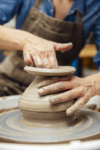Handen van senior vrouwelijke Potter werken op aardewerk wiel terwijl zittend in haar workshop - Foto, afbeelding