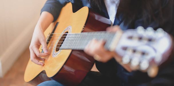 Nahaufnahme einer Frau, die in einem komfortablen Raum akustische Gitarre spielt - Foto, Bild