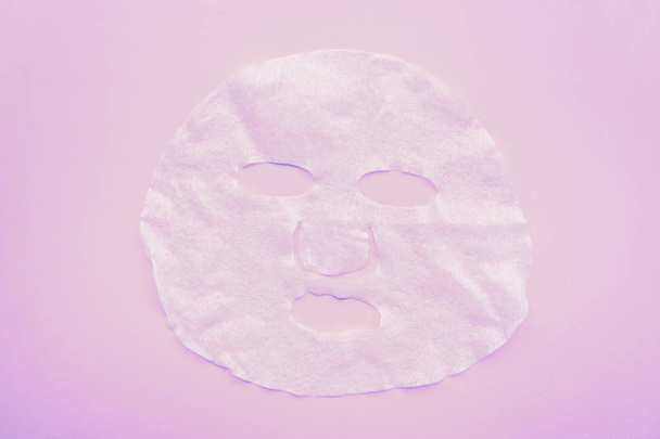 Sheet facial mask on pastel pink paper background. Skin care, dermatology, beauty concept. Top view, flat lay, mockup, overhead, copy space, template - Foto, afbeelding