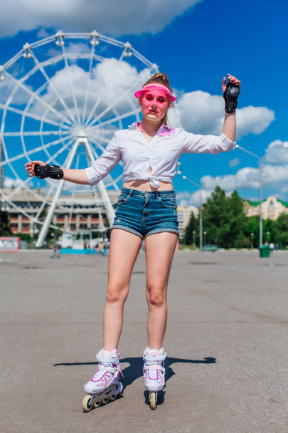 Portrait of an emotional girl in a pink cap visor and protective gloves for rollerblades and skateboarding riding on rollerblades on the road. - Foto, immagini