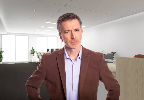 Middle-Aged businessman with gray hair and wearing a brown jacket standing in an office.  Depicts startup and corporate business.  He is looking upset or angry. - Foto, afbeelding