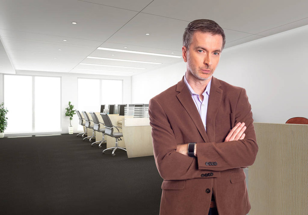 Middle-Aged businessman with gray hair and wearing a brown jacket standing in an office.  Depicts startup and corporate business.  He is looking confident or arrogant. - Foto, afbeelding