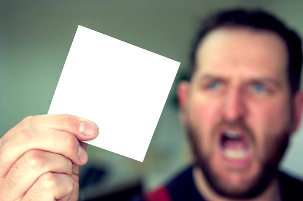 un hombre gritando en el fondo fuera de foco sostiene una hoja en blanco de papel en su mano en el primer plano
 - Foto, Imagen