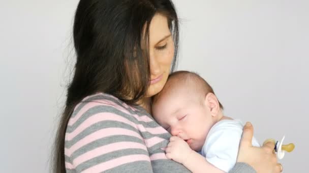 Jonge mooie moeder met lang donker haar houdt een pasgeboren baby van twee maanden op witte achtergrond in Studio - Video