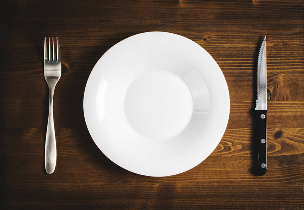 White empty plate with a fork and knife on a wooden table. - 写真・画像