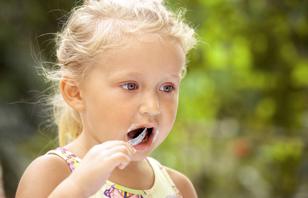 Cute girl child licks a spoon with a delicious ice cream on a co - Photo, Image