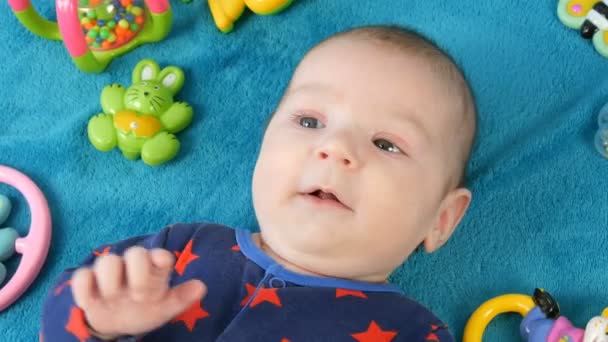 Portrait de beau petit nouveau-né drôle de deux mois couché sur un couvre-lit bleu entouré de hochets de bébé
 - Séquence, vidéo