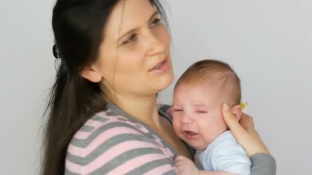 Young beautiful mother with long dark hair is holding a newborn infant baby of two months on white background in studio - Footage, Video