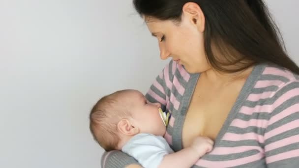 junge schöne Mutter mit langen dunklen Haaren hält ein neugeborenes Baby von zwei Monaten auf weißem Hintergrund im Studio - Filmmaterial, Video