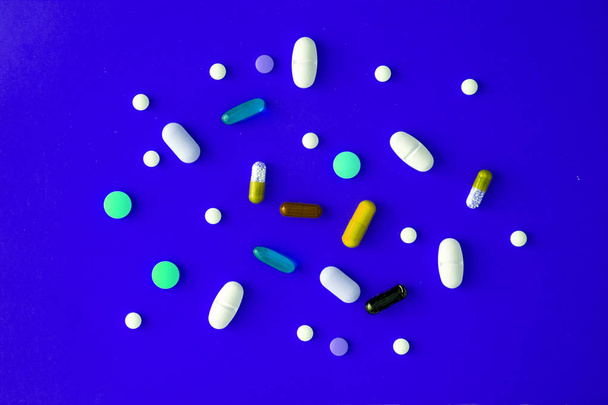 verspreide verschillende gekleurde tabletten in een blauw-cyaan achtergrond. Uitzicht van bovenaf. Close-up - Foto, afbeelding
