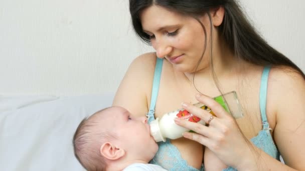Dwa miesiące noworodek leży na ramionach matki i ssie sutek z butelki mleka - Materiał filmowy, wideo