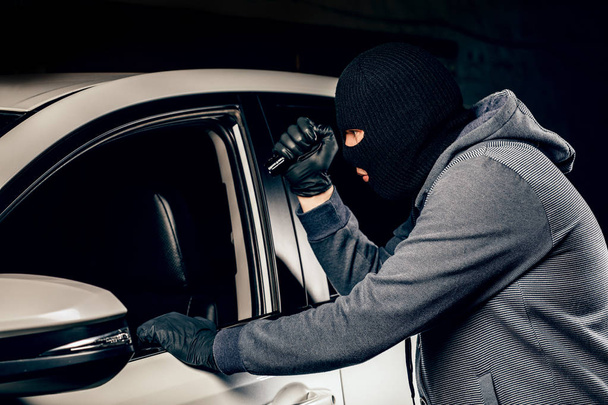 Un ladrón vestido con una máscara negra, apuntando con una linterna al dri
 - Foto, imagen