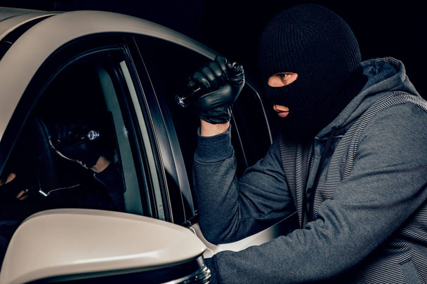 A robber dressed in a black mask, aiming a flashlight at the dri - Photo, Image
