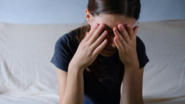 Depressed anxious worried young woman sitting on the sofa crying at home. Depressed frustrated female having emotional problems, fears, worried and hopeless. Psychological therapy, no energy - Footage, Video