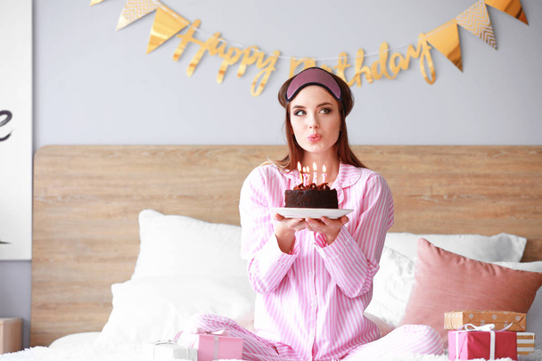 Femme heureuse avec gâteau d'anniversaire assis sur le lit à la maison
 - Photo, image