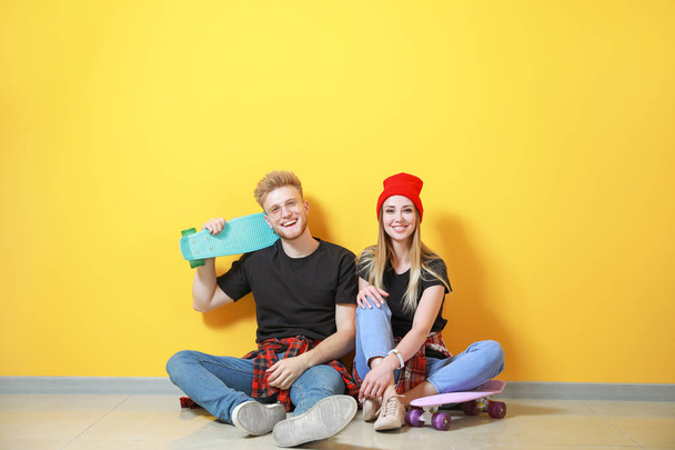 Couple en t-shirts élégants et avec des planches à roulettes assis près du mur de couleur
 - Photo, image