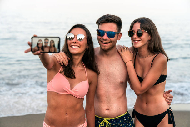 Giovani amici che si fanno selfie sulla spiaggia sul mare dell'oceano insieme
 - Foto, immagini