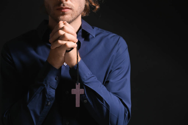 Religious young man praying on dark background - Foto, imagen