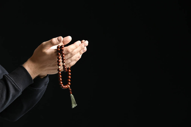 Religious young man praying to God on dark background - Фото, изображение