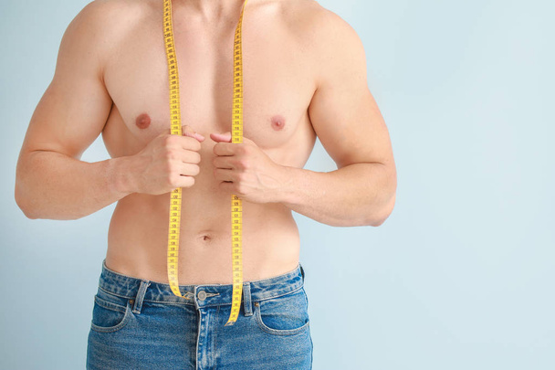 Handsome muscular man with measuring tape on color background. Weight loss concept - Fotó, kép