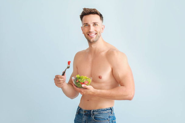 Hezký svalnatý muž se salátem na barevném pozadí. Koncepce ztráty váhy - Fotografie, Obrázek