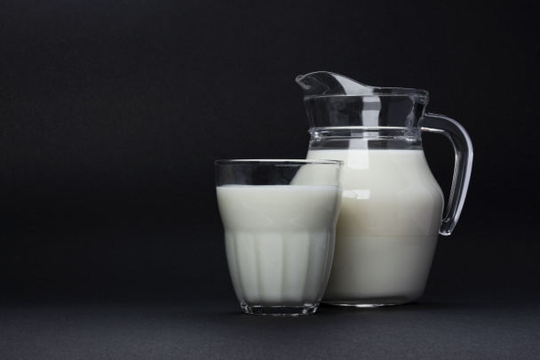 Βάζο και ποτήρι γάλα απομονωμένα σε μαύρο φόντο με χώρο αντιγραφής για κείμενο, έννοια γαλακτοκομικών προϊόντων - Φωτογραφία, εικόνα