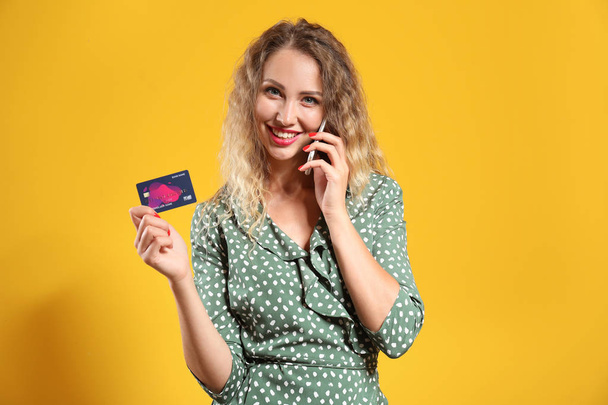 Fiatal nő hitelkártyával beszél mobiltelefonnal a színes háttér - Fotó, kép