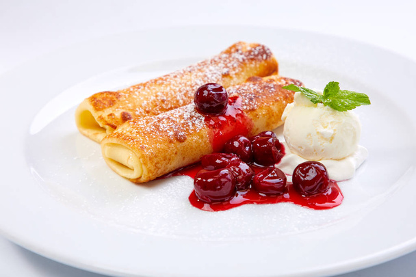 сладкие блинчики с вишней на белой тарелке, крупным планом
  - Фото, изображение