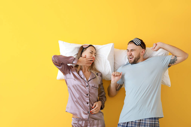 Сонная молодая пара с подушками на цветном фоне
 - Фото, изображение