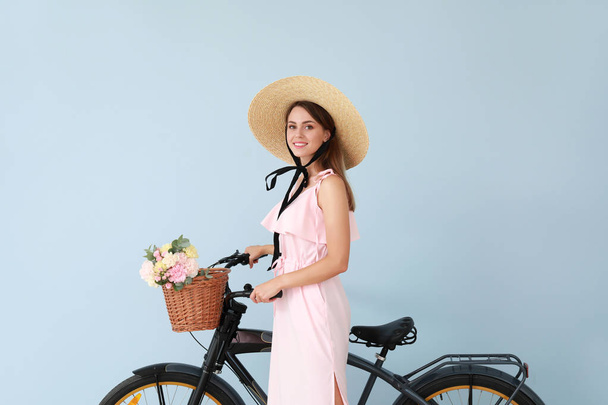 Beautiful young woman with bicycle and bouquet of carnation flowers on color background - Foto, Imagen