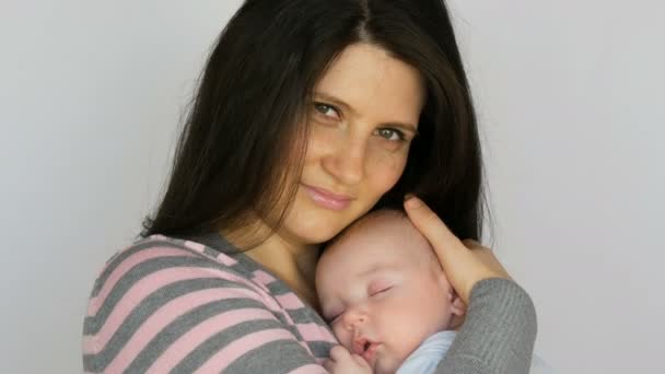 junge schöne Mutter mit langen dunklen Haaren hält ein neugeborenes Baby von zwei Monaten auf weißem Hintergrund im Studio - Filmmaterial, Video