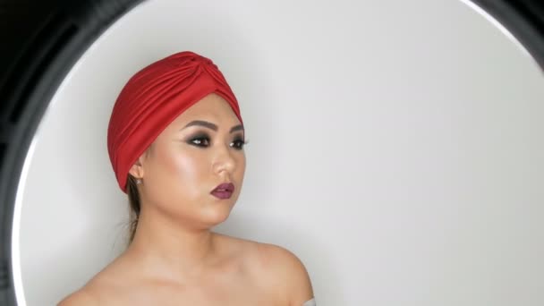 Beautiful Korean Asian girl in a trendy red turban with bright evening make-up smoky eyes posing in studio on a white background - Footage, Video
