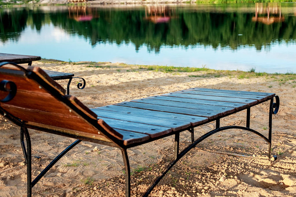 Dinlenme bölgesi. Ahşap şezlong lar ve masalar ile sandalyeler göl eteklerine bakan, göl kenarında ki plajda duruyor. - Fotoğraf, Görsel