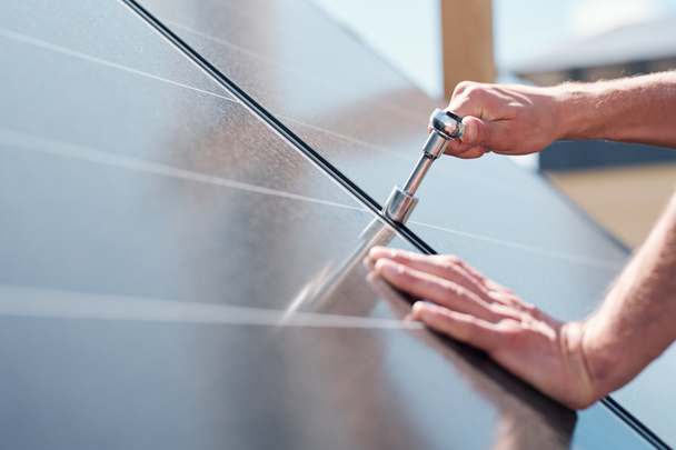 Hands of contemporary master with screw adjusting or installing solar panels on rooftop of house - Photo, Image