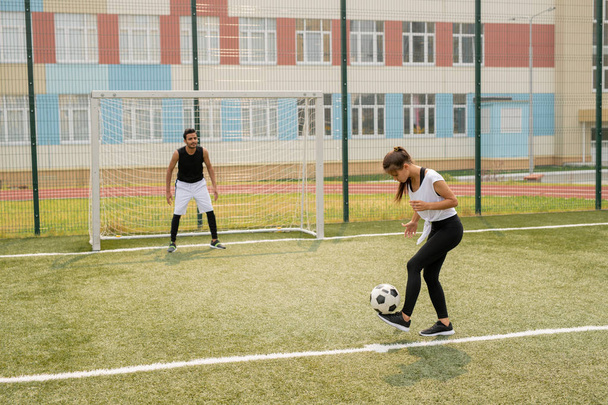 Young female in sportswear standing on soccer field while learning to play with sportsman on background - Photo, Image
