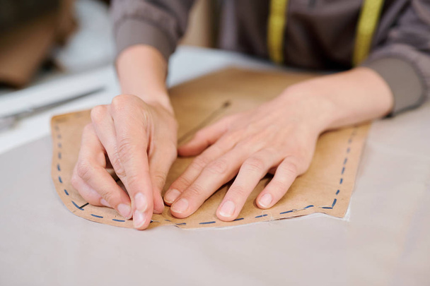 Jonge vrouwelijke kleermaker vastmaken papierwerk stuk aan stukje stof voordat het schetsen en snijden - Foto, afbeelding