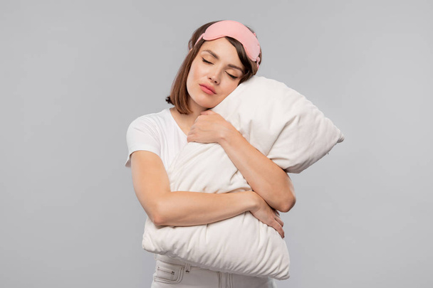 Stüdyoda fotoğraf çekimi sırasında başını üzerinde tutarken yastık kucaklayan genç sakin kadın - Fotoğraf, Görsel