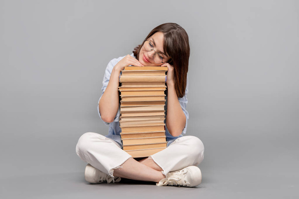Mulher inteligente stuudent ou bibliotecário com pernas cruzadas mantendo a cabeça no topo dos livros enquanto sonha em lê-los todos
 - Foto, Imagem