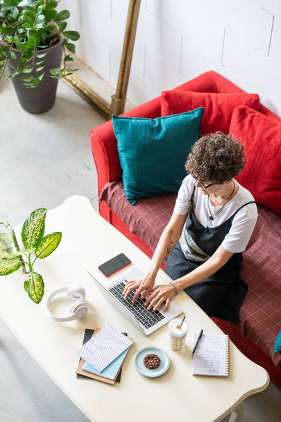 Jovem gerente de escritório feminino trabalhando remotamente na frente do laptop enquanto sentado à mesa em ambiente doméstico
 - Foto, Imagem