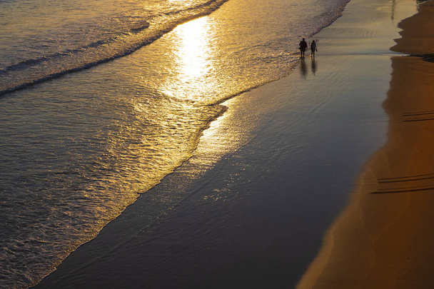 Two people walking along the shore of La Concha beach at sunrise, city of Donostia - Fotoğraf, Görsel
