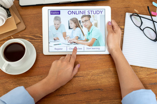 Mãos de jovem segurando tablet digital ao tocar em um dos botões na página inicial do site educacional
 - Foto, Imagem