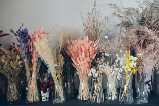 Achtergrondafbeelding van kleurrijke pluizige gedroogde bloemen in glazen vazen geplaatst op plank - Foto, afbeelding