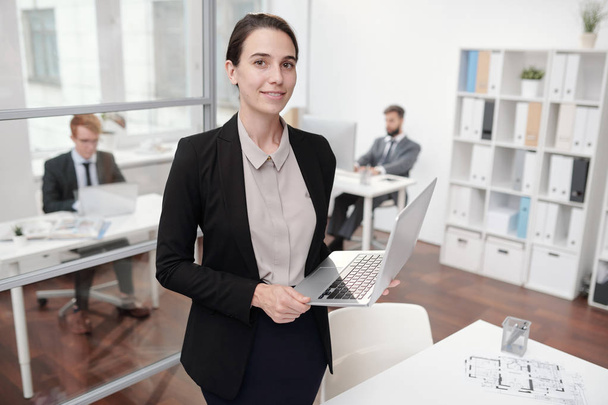 Портрет элегантной молодой бизнесвумен, стоящей в офисе и смотрящей в камеру, копировальное пространство
 - Фото, изображение