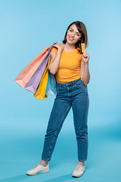 Young casual shopaholic with paperbags showing you credit card while standing in front of camera in isolation - Фото, зображення