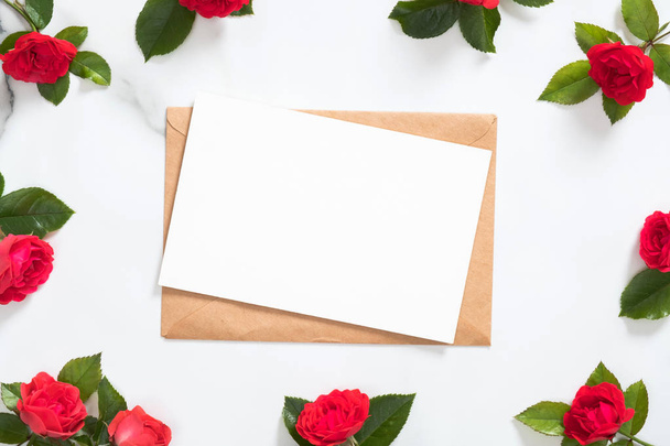 Mockup postcard with craft paper envelope and rose flowers frame on marble background. Minimal style composition, flat lay, view from above. Romantic love letter concept. - Photo, image