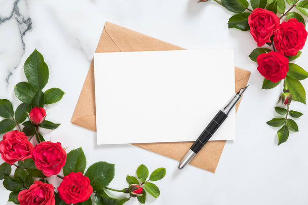 Mockup postcard with craft paper envelope, pen and rose flowers frame on marble stone background. Minimal style composition, flat lay. top view. Love letter concept. - 写真・画像