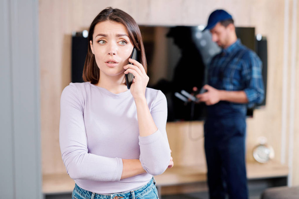 Młody martwi kobieta wzywając swojego przyjaciela, aby skonsultować się o podziale Panel plazmowy z repairman na tle - Zdjęcie, obraz
