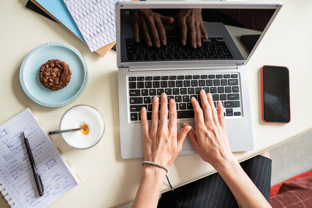 Overzicht van menselijke handen op laptop toetsenbord tijdens netwerk per bureau in thuisomgeving - Foto, afbeelding