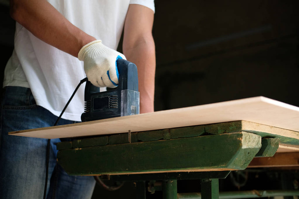 Ο ξυλουργός πριονίζει ένα φύλλο κόντρα πλακέ με μηχανή πριονιού στο εργαστήρι ξυλουργικών. Πλευρική όψη. DIY ιδέα. - Φωτογραφία, εικόνα